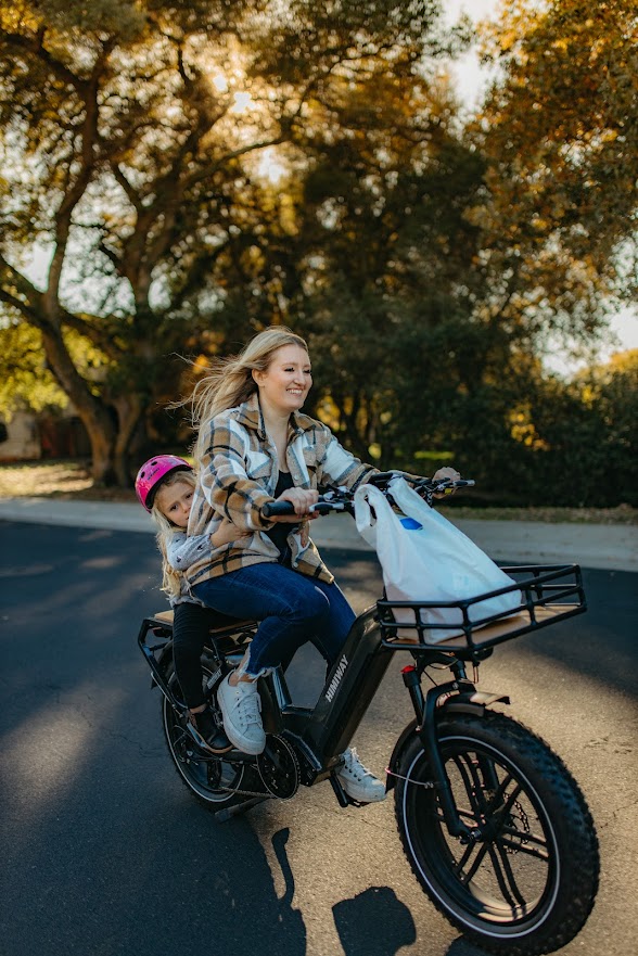 Girl riding an electric bike with little baby girl sitting behind.