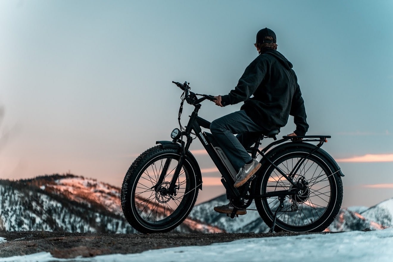Man sitting on electric bicycle on top of snowy mountain.